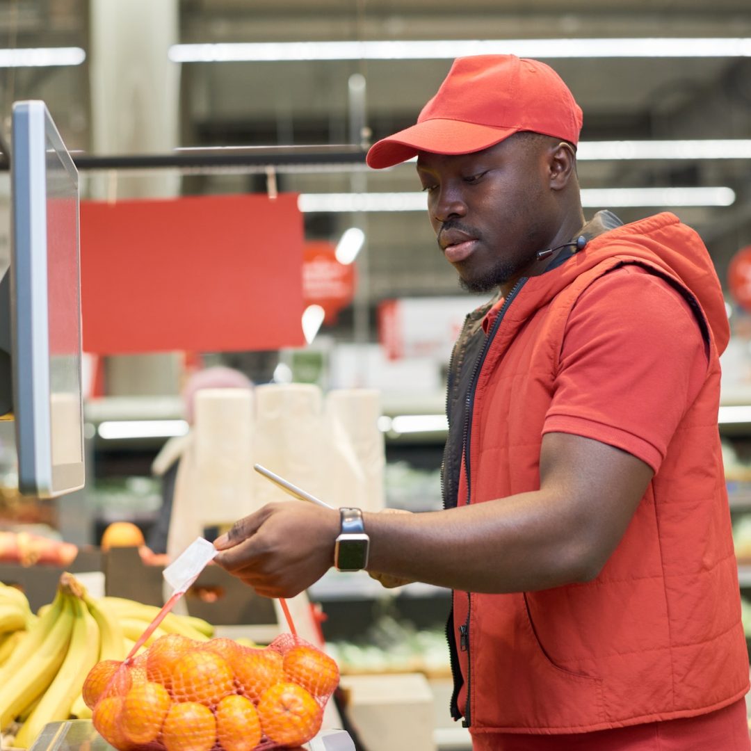 Young African American worker of supermarket weighing pack of mandarins